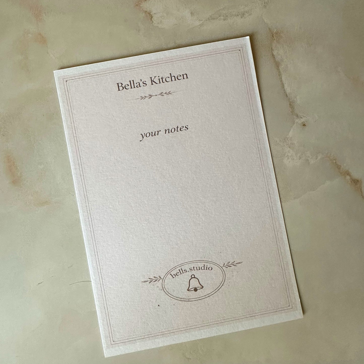 Notebook with 'Bella's Kitchen' branding on a marble surface